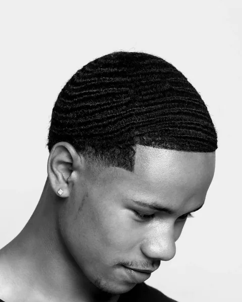 A young man looking down, with waves on top and a sharp shape-up along the hairline.