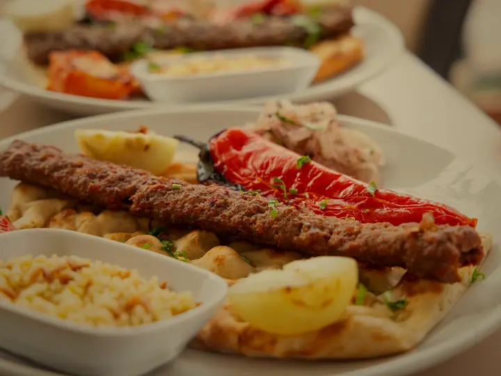 A long kofta kebab on flatbread with a roasted red pepper, rice and lemon.