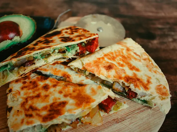 Golden quesadilla wedges stacked on a dark wooden board.