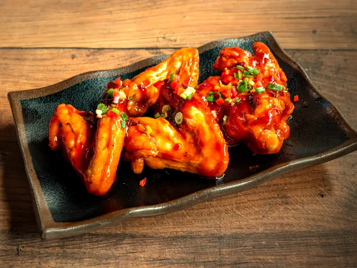 Glossy sauced chicken wings with chilli and scallions on a black slate.
