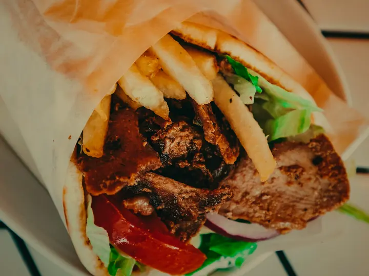 A shawarma wrap opened at the top, packed with sliced meat, fries, tomato and lettuce.